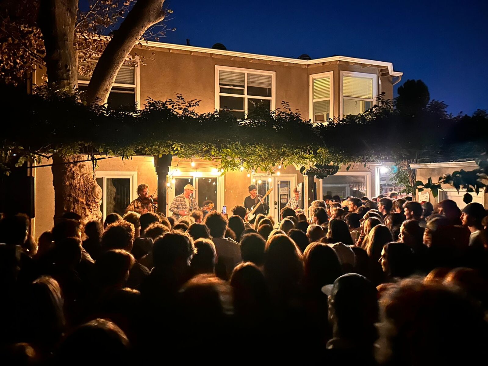 A band playing a backyard show at night for a packed crowd