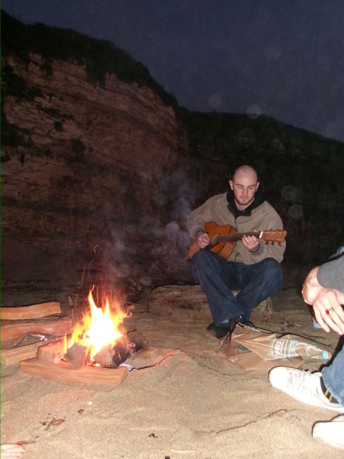 Playing acoustic guitar by a campfire on the beach
